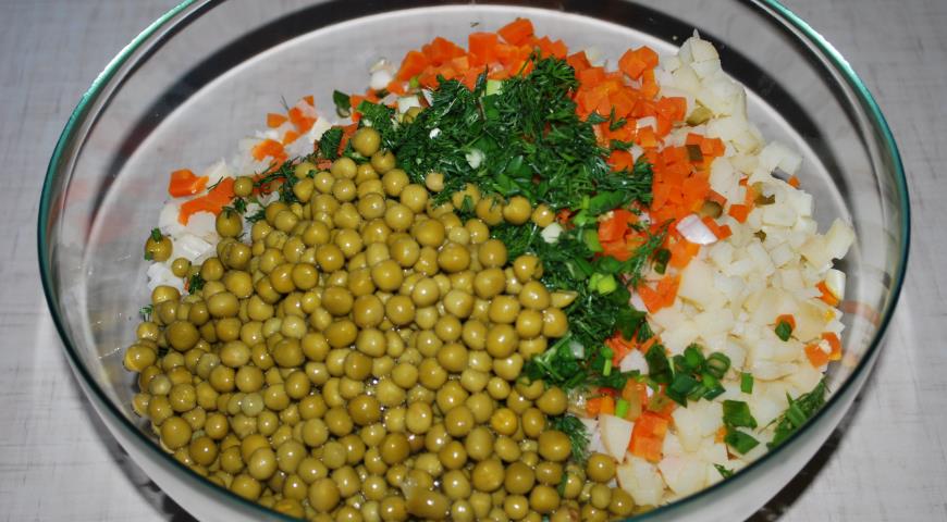 В миску с овощами для оливье добавить зеленый горошек, зелень, соль и черный перец, добавить майонез